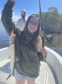 A young angler proudly displaying a Snook caught while fishing on a boat in a scenic waterway.