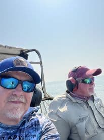 Two anglers enjoying a day on the water, seated inside the boat with a clear view of the ocean.