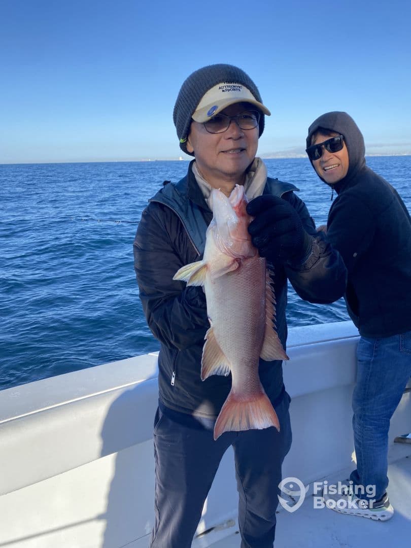 An angler proudly displaying a large Snapper while fishing on a boat in open waters.