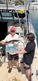 Two anglers proudly displaying their catch, a Barracuda and a Mahi Mahi, on the deck of a fishing charter boat.