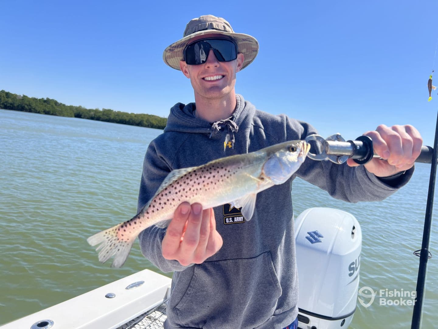 Angler proudly displaying a Speckled Trout while fishing in a scenic coastal environment.