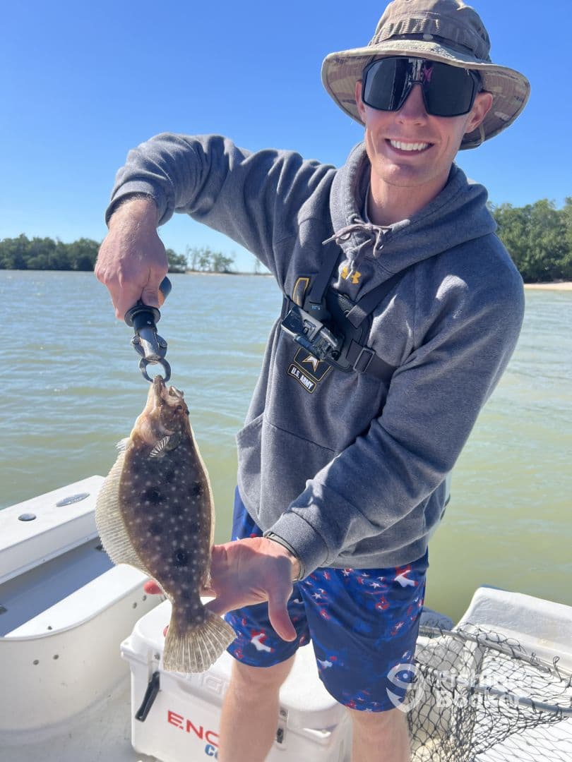 Angler proudly displaying a Flounder while fishing from a boat in a coastal environment.