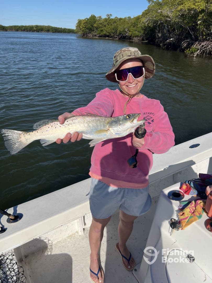 Angler proudly displaying a large Speckled Trout while fishing in a scenic mangrove area.