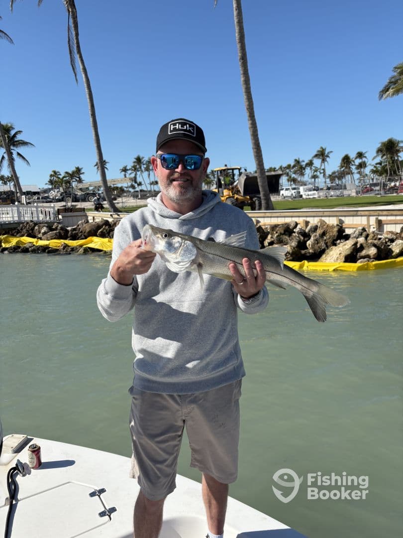 An angler proudly displaying a Snook caught while fishing from a boat in a sunny coastal environment.