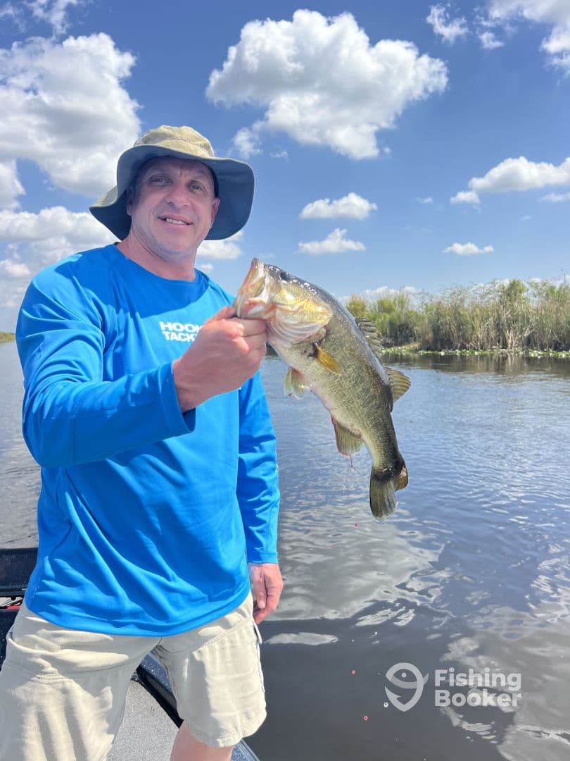 An angler proudly displaying a large Largemouth Bass while fishing in a scenic freshwater environment.