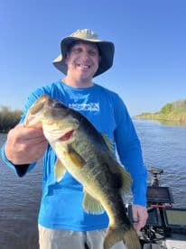 An angler proudly displaying a large Largemouth Bass while fishing in a serene waterway, showcasing a successful day on the water.