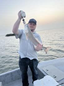 Angler proudly displaying a large Redfish while fishing from a boat in a coastal waterway during sunset.