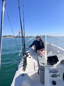 A young woman enjoying a sunny day aboard a fishing boat, equipped with fishing rods and a scenic view of the coastline.