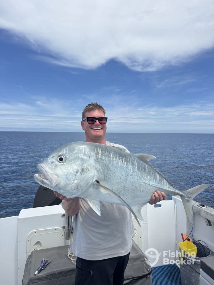 Angler proudly displaying a large Trevally while fishing offshore, showcasing a beautiful day on the water.