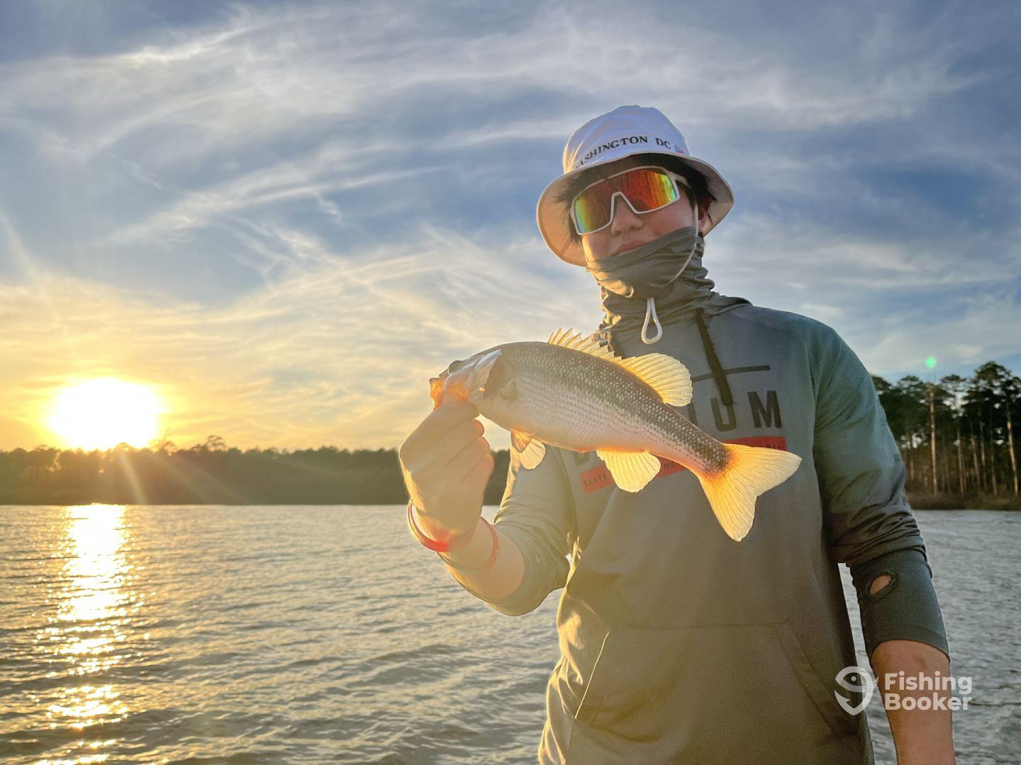 A young angler proudly displaying a freshly caught Largemouth Bass during a sunset fishing trip on a serene lake.