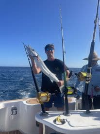 An angler proudly displaying a large Barracuda while fishing on a charter boat in open waters.