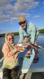 Two anglers proudly displaying a large fish on a boat in a scenic fishing environment.