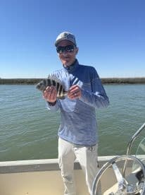 An angler proudly displaying a Sheepshead caught while fishing on a boat in calm waters.