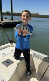 A young angler proudly displaying a Black Drum caught while fishing from a boat in a calm waterway.