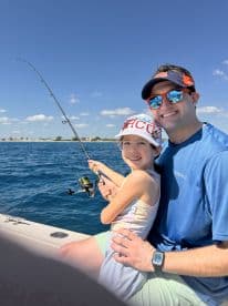 A young girl and her father enjoying a fishing trip together, with the girl actively reeling in her line on a sunny day.