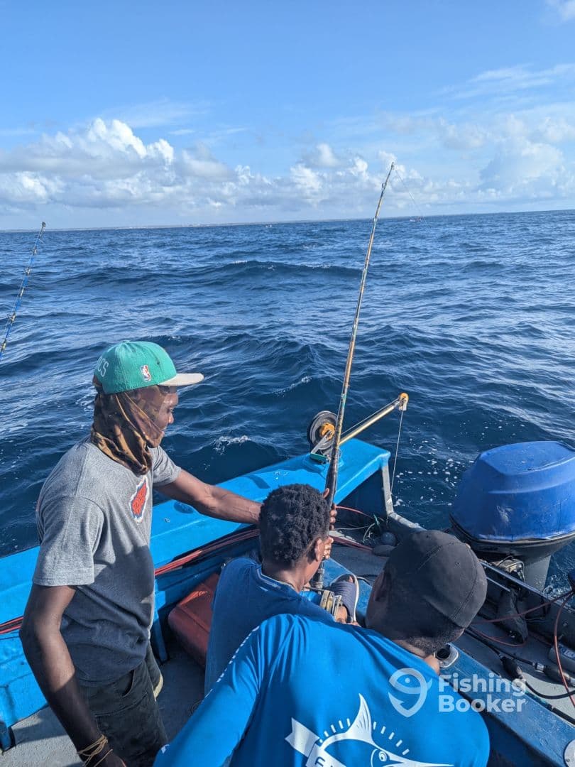 Three anglers engaged in fishing on a small boat, with one actively reeling in a catch amidst a scenic ocean backdrop.
