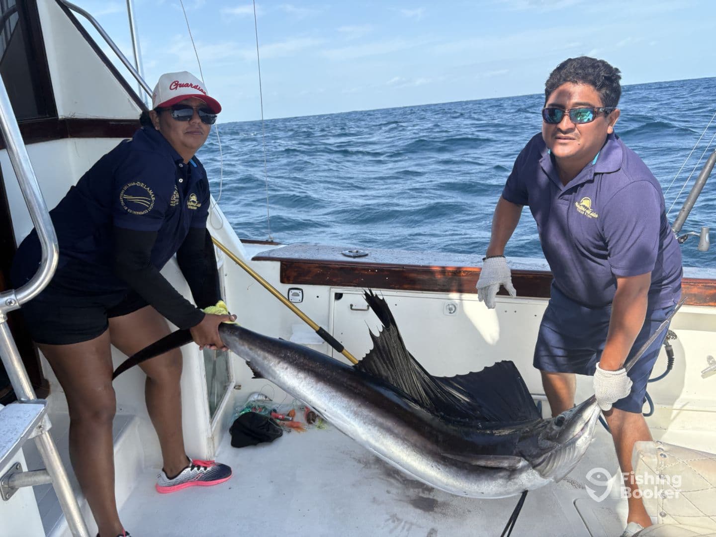 Two anglers proudly displaying a large Sailfish aboard a sportfishing boat in open waters.