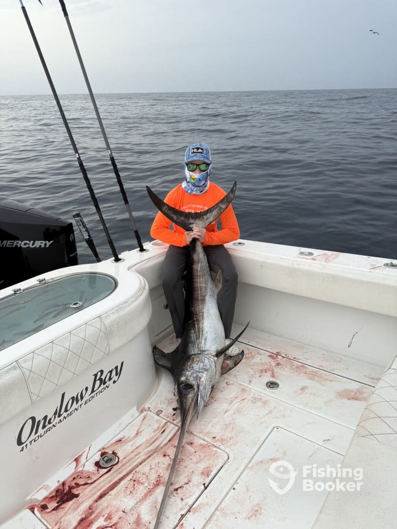 Young angler proudly displaying a large Swordfish aboard an Onslow Bay boat during a deep-sea fishing trip.