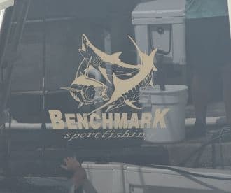 The exterior of the Benchmark sportfishing boat, showcasing its logo and a glimpse of the fishing environment.