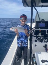 A young angler proudly displaying a fish on a boat during a fishing trip in open waters.