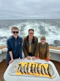 A family of three proudly displaying their catch of several fish on a boat after a successful fishing trip.