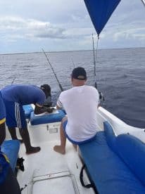 Two anglers aboard a small fishing boat, preparing for a fishing trip in open waters, with rods set up and a relaxed atmosphere.