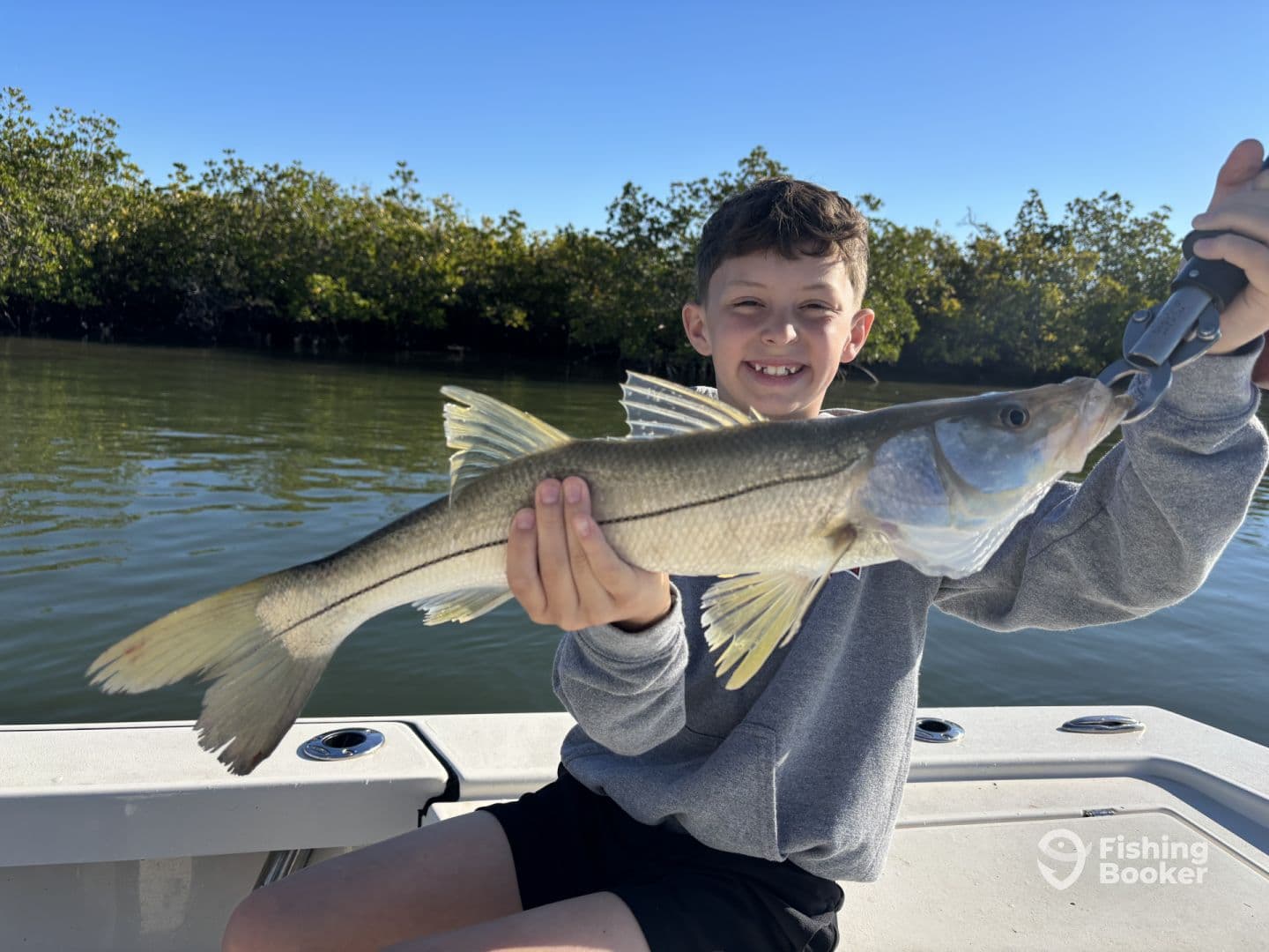 A young angler proudly displaying a Snook while fishing in a mangrove-lined waterway.