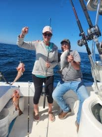 Two anglers proudly displaying their catch, including a large Snapper and a Grouper, while fishing on a sunny day in open waters.