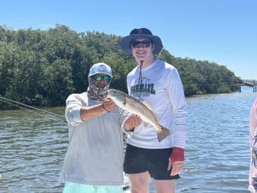 Two anglers proudly displaying a Redfish while fishing in a scenic coastal environment.