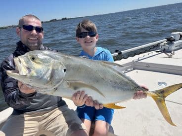 A young angler and his father proudly display a large Jack Crevalle while fishing on a sunny day.