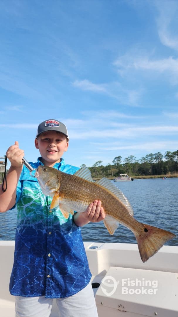 Young angler proudly holding a large Redfish while fishing on a sunny day.