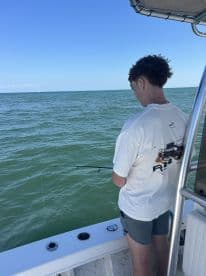 A young angler is focused on fishing from a boat in clear waters, showcasing the excitement of the fishing experience.