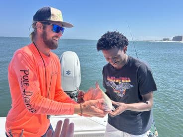 Two anglers on a boat enjoying a successful fishing trip, showcasing a vibrant Red Snapper caught in coastal waters.
