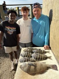 A group of anglers proudly displaying their catch of striped bass and other species on a board after a successful fishing trip.