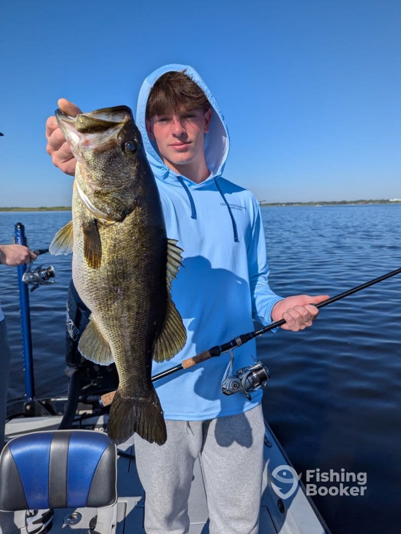 A young angler proudly displaying a large Largemouth Bass while fishing on a sunny day.