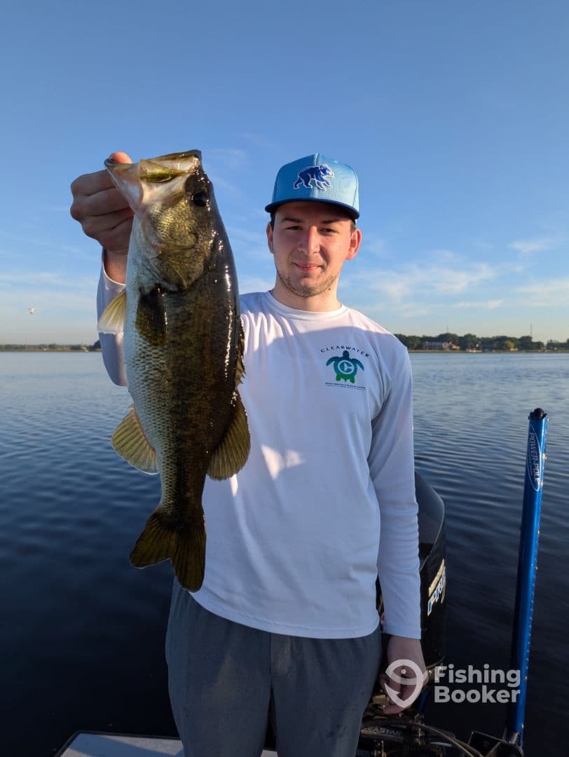 An angler proudly displaying a large Largemouth Bass while fishing on a calm lake, showcasing a beautiful morning fishing experience.