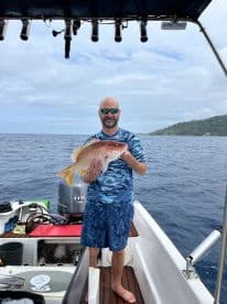 An angler proudly displaying a large Snapper while fishing on a boat in open waters.