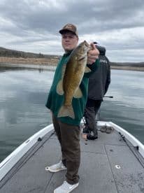 Angler proudly displaying a sizable Smallmouth Bass while fishing on a calm lake, showcasing a successful day on the water.