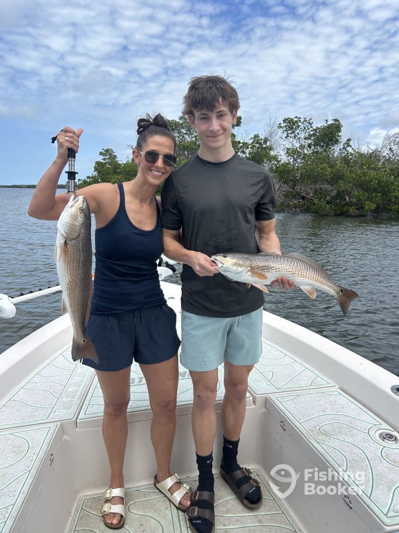 A young angler and an adult proudly displaying their catches of Redfish while on a fishing trip in a scenic coastal environment.