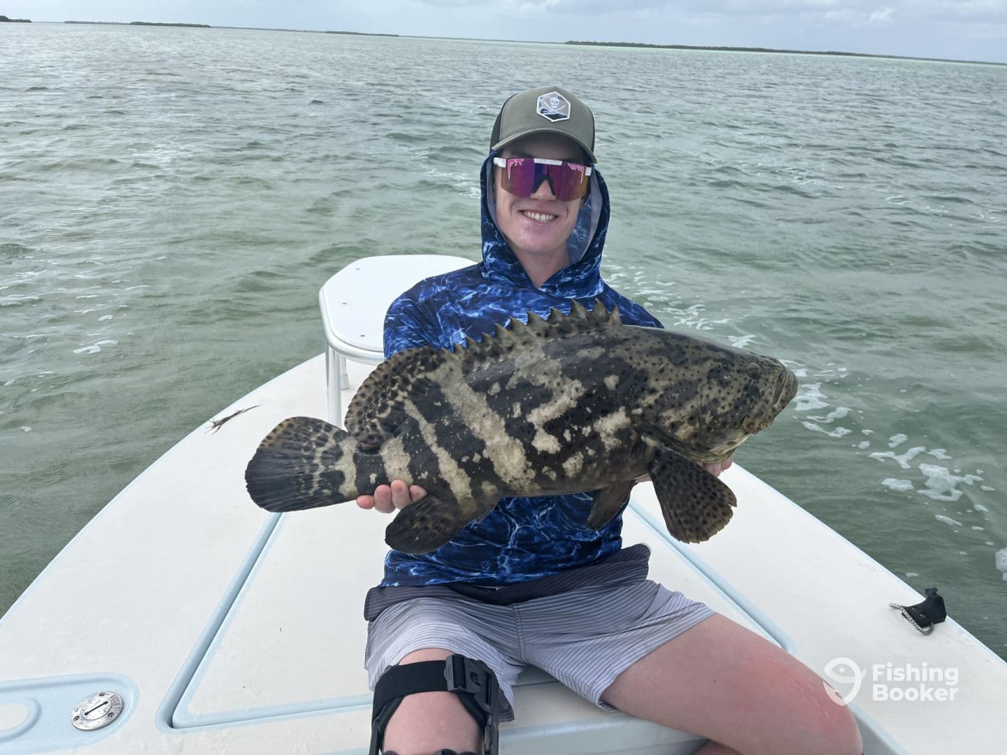 An angler proudly displaying a large Goliath Grouper while fishing in a coastal environment.