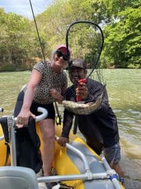 Two anglers proudly displaying their catch while enjoying a day on a river in a yellow inflatable boat.