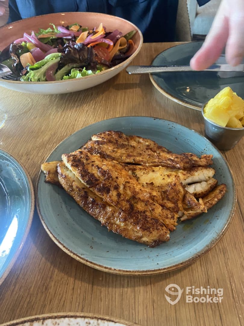 A plate featuring grilled fish fillets accompanied by a fresh salad and a side of fruit, likely enjoyed at a restaurant.