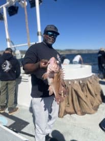 Angler proudly displaying a colorful Rockfish while fishing on a charter boat, showcasing a successful day on the water.