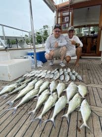 Two anglers posing next to a large catch of Yellowtail Snapper on the deck of a boat, showcasing a successful fishing trip.