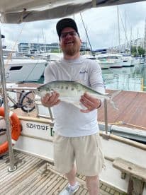 An enthusiastic angler proudly displaying a large fish on the deck of a boat, surrounded by a marina setting.