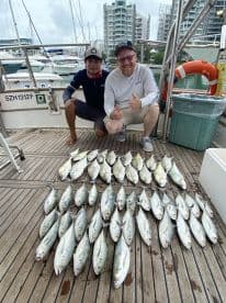 Two anglers posing with a large catch of fish on the deck of a boat, showcasing a successful fishing trip.