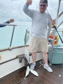 Angler reeling in multiple fish, including a Mackerel, while fishing from a charter boat in clear waters.