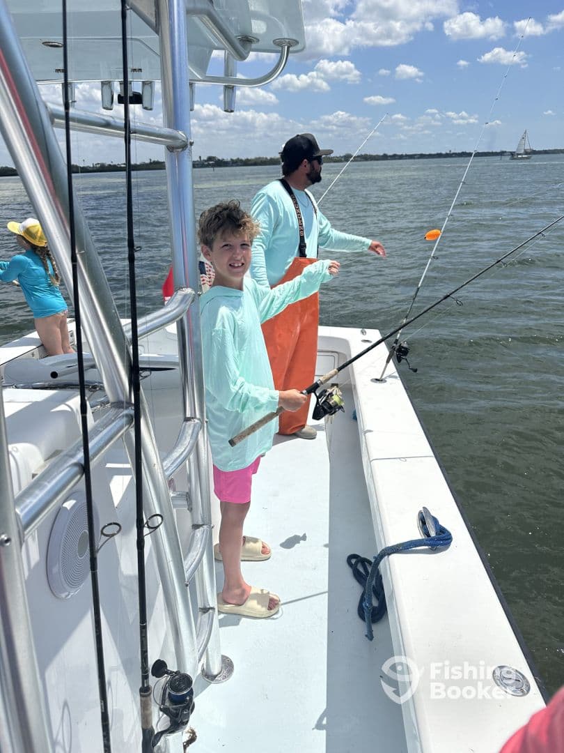 A young angler is actively fishing from a boat, enjoying a sunny day on the water with family members in the background.