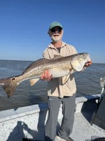 An angler proudly displaying a large Redfish while fishing on a boat in open waters.