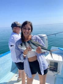 A happy angler proudly displaying a caught fish while fishing on a boat in calm waters.
